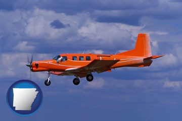 a red turboprop aircraft flying in a blue sky with cumulus clouds - with Arkansas icon