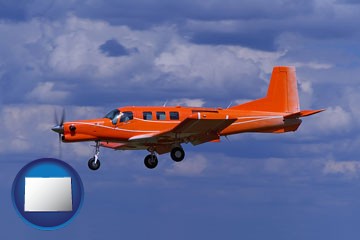 a red turboprop aircraft flying in a blue sky with cumulus clouds - with Colorado icon