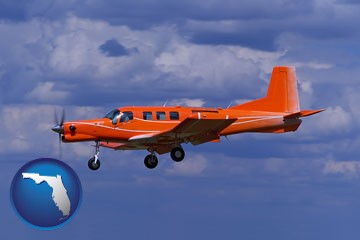 a red turboprop aircraft flying in a blue sky with cumulus clouds - with Florida icon