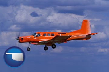 a red turboprop aircraft flying in a blue sky with cumulus clouds - with Oklahoma icon