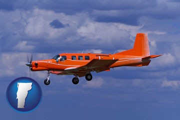 a red turboprop aircraft flying in a blue sky with cumulus clouds - with Vermont icon