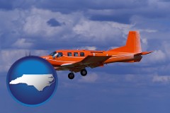 north-carolina map icon and a red turboprop aircraft flying in a blue sky with cumulus clouds