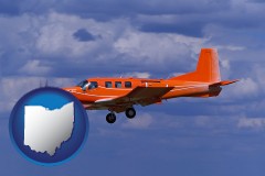 ohio map icon and a red turboprop aircraft flying in a blue sky with cumulus clouds