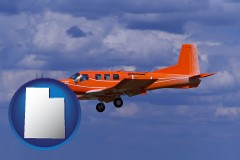 utah map icon and a red turboprop aircraft flying in a blue sky with cumulus clouds